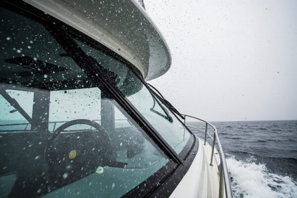 Professional marine wiper blades actively clearing heavy rain and salt spray from a boat windshield during stormy weather, demonstrating the critical importance of clear visibility for safe navigation.