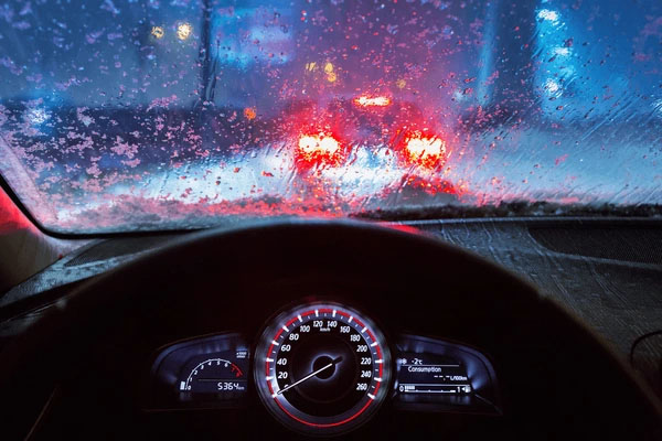 Close-up of a car’s ADAS camera behind a dirty windshield with streaks caused by old wipers.