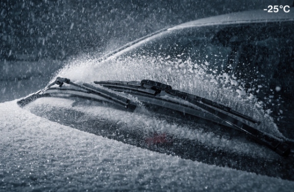 Silicone wiper blades powerfully clearing heavy snow and ice on a frozen windshield in extreme winter conditions